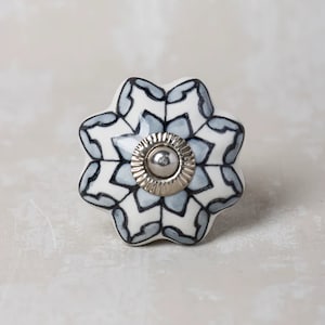 Peut inclure: Un bouton en céramique blanche avec un motif géométrique bleu et noir. Le bouton a un centre en métal argenté.