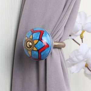 May include: Blue and red ceramic curtain tieback with a gold star design. The tieback is attached to a brown metal rod.