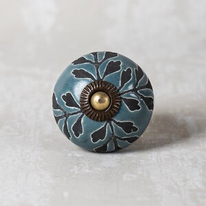 May include: A blue ceramic knob with a black floral design and a brass accent. The knob is round and has a smooth surface.