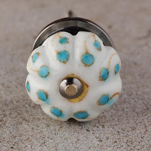 Puede incluir: Pomo de cerámica blanco con un diseño floral azul y dorado. El pomo tiene una base de metal plateado.