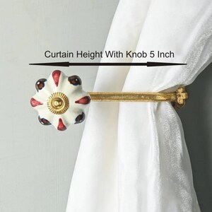 May include: Gold curtain rod with a white ceramic knob with red and blue accents. The knob is 5 inches tall and the rod extends 2 inches from the wall.