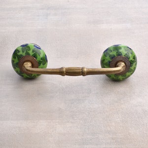 May include: A brass cabinet pull with two green and blue ceramic knobs. The knobs have a floral pattern.