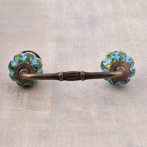 May include: A blue and green ceramic drawer pull with a brass arm. The pull has a floral pattern and a slightly raised edge.