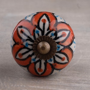 Può includere: Un pomello in ceramica con un design floreale in tonalità arancio, bianco e nero. Il pomello ha una base in metallo color ottone.