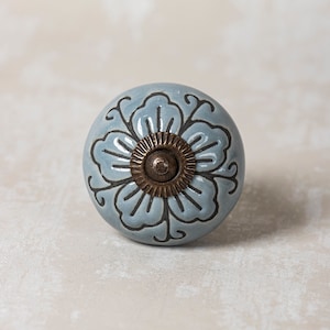 Peut inclure: Un bouton en céramique bleu avec un motif floral blanc et une vis en laiton. Le bouton est rond et a une surface lisse.