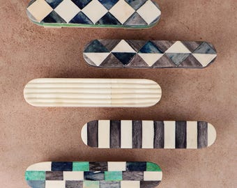 May include: Five elongated, oval-shaped decorative objects arranged vertically. The top two feature blue and white diamond patterns. The middle one is solid cream with horizontal ridges. The bottom two display black and white stripes and a green, blue, and white checkered pattern.