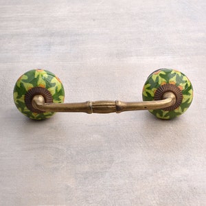 May include: A brass drawer pull with two green and yellow ceramic knobs. The knobs have a floral pattern.