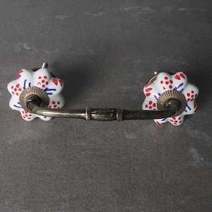 以下が含まれることがあります： 赤と青のドット模様の白いセラミック製の引き出しの取っ手と真鍮製の棒。