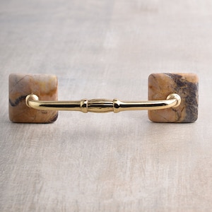 May include: A gold-toned cabinet pull with square, marbled handles. The handles are a light brown with dark brown and grey streaks.