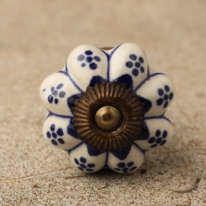 May include: White ceramic knob with a blue floral pattern and a gold metal center. The knob has a scalloped edge.