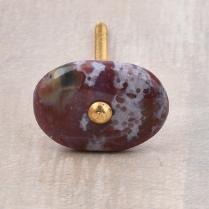 Op de afbeelding: Een bruine en witte agaten knop met een gouden schroef. De knop is ovaalvormig en heeft een gevlekt patroon.