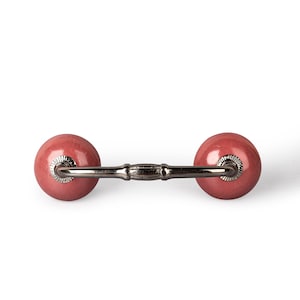 May include: A red ceramic drawer pull with a silver metal bar connecting the two round knobs.