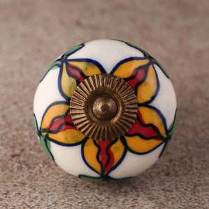May include: A white ceramic knob with a yellow, red, and green floral design. The knob has a brass base.