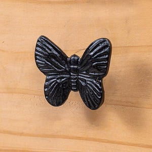 Op de afbeelding: Zwarte metalen vlinder-ladegreep. De vlinder heeft gedetailleerde vleugels en een gestructureerde afwerking.