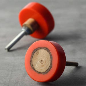 Könnte beinhalten: Zwei runde rote Schrankknöpfe mit einem Holzeinlegeteil. Ein Knopf ist scharf gestellt, der andere unscharf.