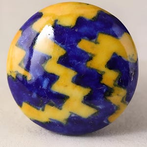 Può includere: Un pomello rotondo in ceramica con un motivo geometrico blu e giallo. Il pomello ha una finitura lucida.