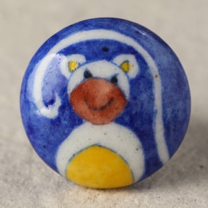 May include: A blue and white ceramic knob featuring a cartoon animal design. The animal has a white body, yellow ears, and a red mouth.