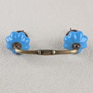 May include: A blue ceramic drawer pull with a brass bar connecting two knobs. The knobs are shaped like a flower with a raised center.
