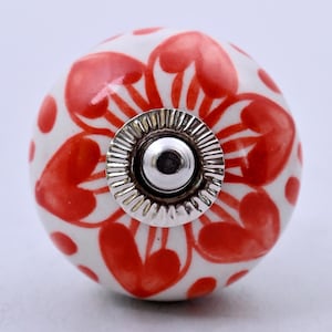 May include: A round ceramic cabinet knob featuring a white base with a hand-painted red floral pattern. The center of the knob has a polished silver-tone metal hardware fitting with a ridged circular edge and a central screw hole.