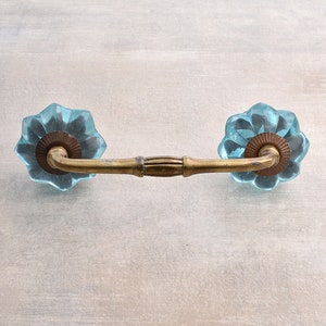 May include: A pair of blue glass cabinet knobs with a brass base and a decorative floral design.