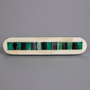 May include: A rectangular, white, bone-like drawer pull with a mosaic of green and black squares.