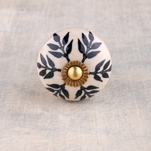 May include: White ceramic knob with a black floral design and a gold centre.