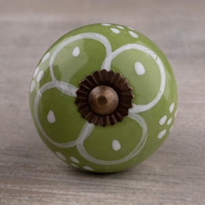 May include: Green ceramic knob with a white floral design and a brass screw. The knob has a round shape and a smooth surface.