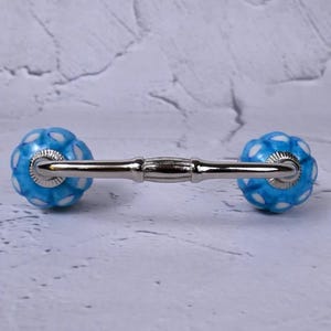 May include: A cabinet pull with a silver handle and blue ceramic knobs. The knobs are decorated with a white floral pattern. This decorative hardware is suitable for drawers and cabinets.
