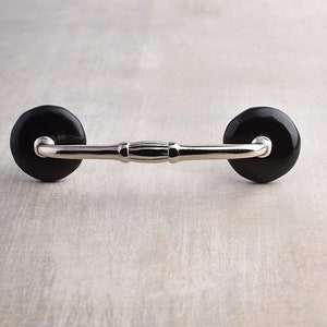 May include: A black ceramic drawer pull with a silver metal arm. The pull has a simple, elegant design.