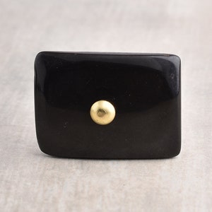 May include: Black rectangular cabinet knob with a gold metal centre.