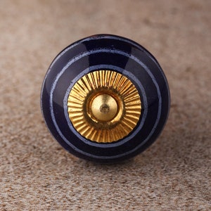 May include: A blue and white striped ceramic knob with a gold center. The knob is round and has a smooth surface.