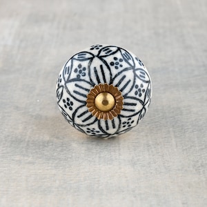 May include: White ceramic knob with a black and white floral pattern and a gold metal center.