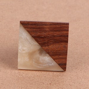 Peut inclure: Une bague carrée en bois et résine blanche avec une fente diagonale. Le bois est brun foncé avec un grain de bois naturel. La résine est d'un blanc clair avec une finition chatoyante.