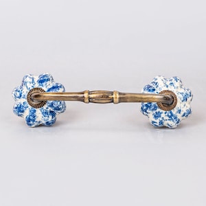 May include: A blue and white ceramic drawer pull with a brass bar connecting the two sides. The ceramic is patterned with a blue and white floral design.