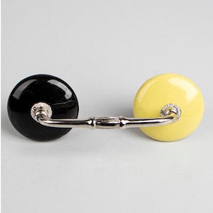 Op de afbeelding: Een zwarte en gele keramische ladegreep met een zilveren metalen verbindingsstang.