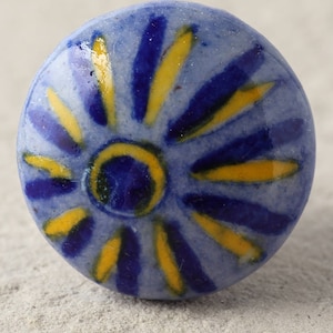 Op de afbeelding: Een blauwe keramische knop met een geel en blauw bloemenmotief. De knop is rond en heeft een glad oppervlak.