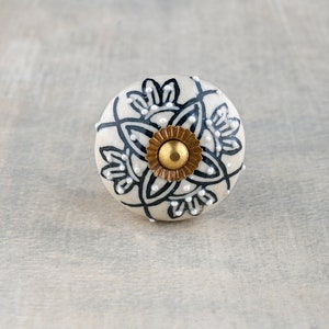 Może przedstawiać: Biały ceramiczny gałka z czarno-białym wzorem kwiatowym i złotym środkiem.