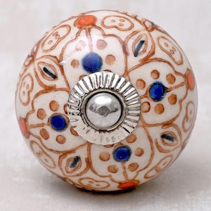 Puede incluir: Pomo de cerámica blanco con un patrón floral marrón y acentos azules y naranjas. El pomo tiene una base de metal plateado.