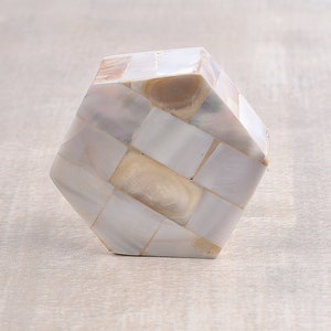 May include: A hexagonal shaped cabinet knob made of white and beige mother of pearl tiles.