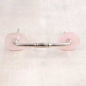 May include: A silver drawer pull with two pink, round, decorative knobs. The knobs are made of rose quartz.