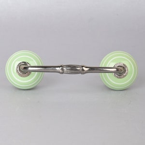 May include: A light green ceramic drawer pull with white stripes and a silver metal bar connecting the two knobs.