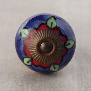 Może przedstawiać: Niebieski ceramiczny gałka z czerwonym wzorem kwiatu i mosiężnym środkiem. Gałka ma błyszczące wykończenie.