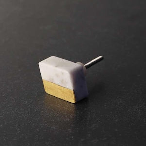 May include: A cabinet knob featuring a white marble top and a gold-coloured base. The knob has a rectangular shape and a metal stem. The design is modern and minimalist, suitable for various furniture styles.