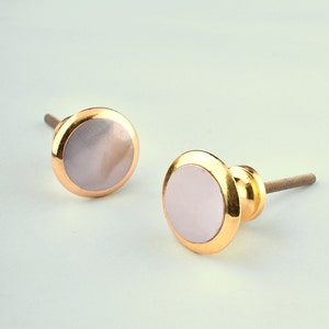 May include: Two gold cabinet knobs with a white mother of pearl inlay. The knobs have a round shape and a screw on the back.