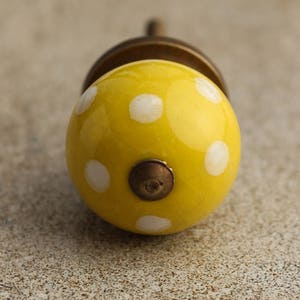 May include: Yellow ceramic knob with white polka dots. The knob has a brass base.
