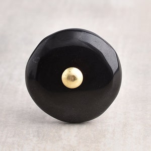 May include: Black round cabinet knob with a gold centre.