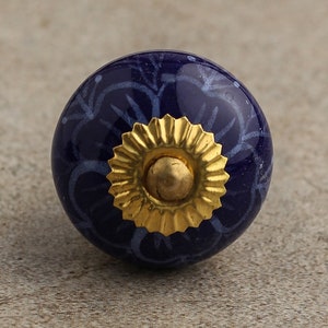 May include: A blue ceramic knob with a white floral pattern and a gold metal base.