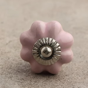 May include: A pink ceramic cabinet knob with a silver metal center. The knob is shaped like a flower with five petals.