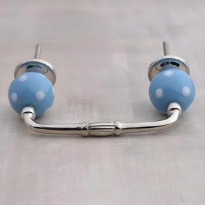 Puede incluir: Un pomo de armario de cerámica azul con lunares blancos y una manija de metal plateado en forma de bucle.