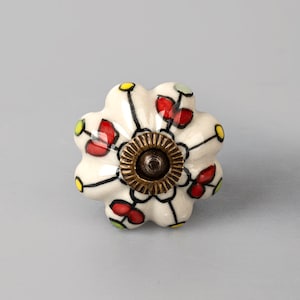 May include: White ceramic knob with a floral design in red, yellow, and green. The knob has a brass center.